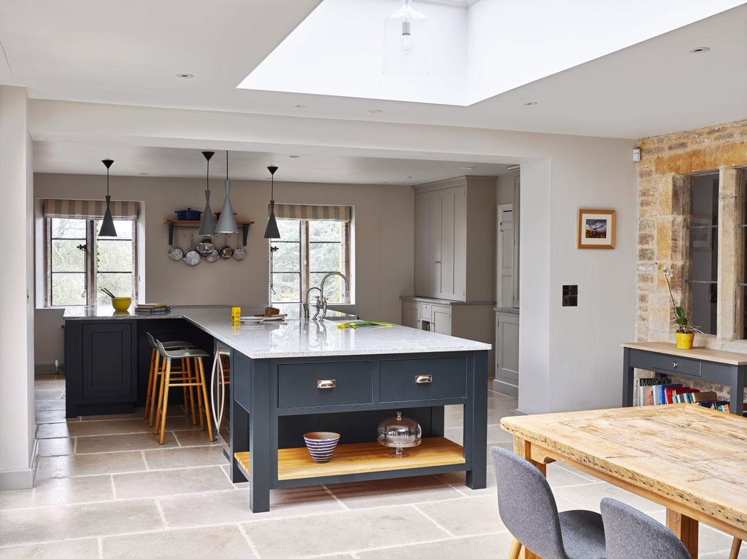 A navy hand-built island kitchen by Stroud Furniture Makers on a Cotswold-stone floor with an exposed dressed-stone wall